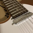 Detail elektrické kytary s bílým tělem a hnědým hmatníkem. Je vidět jeden chromovaný humbucker s kovovým krytem. Na fotce nejsou žádné čitelné značky…