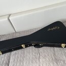 Černý tvrdý kufr na kytaru s rukojetí a kovovými zámky. Na horní části je zlatý nápis Epiphone. Povrch kufrů vykazuje mírné opotřebení v podobě drobn…