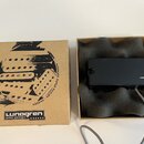 Kartonová krabice s černým potiskem a nápisy „Lunogren guitar pickups“ a „HANDMADE GUITAR PICKUPS · SWEDEN“. Vedle krabice je otevřené balení s černý…