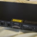 Zadní strana černého rackového zařízení s kovovým povrchem. Na zadním panelu jsou různé konektory a nápisy, včetně označení TASCAM MODEL NO. CD-500B,…