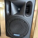 Černý reproduktor v plastovém provedení s horním tubusem pro výsværk. V dolní části je kovová mřížka s modrým logem a nápisem DEXON professional line…