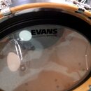 Fotografie zachicuje průhlednou bubnu na bubnu s dřevěným obručem. Na bubně je černý nápis EVANS a pod ním menší text EMAD2. Povrch bubny je čistý, b…