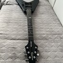 Černá elektrická kytara s tělem ve tvaru V. Na hlavě je bílý nápis Epiphone a na hřdelníku nápis lightningbolt. Kytara má černý hmatník s bílými tečk…