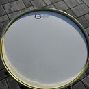 Fotografie zachycuje pohled shora na bílý buben s kovovým obručem. Na povrchu blány je vidět logo a nápis AQUARIAN TEXTURE COATED™. Povrch blány je č…
