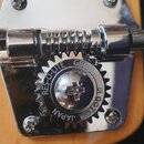 Detail ladicích kolíků na hlavě kytary s kovovým povrchem. Na jednom z kolíků je viditelný nápis RES-O-LITE GB0640 GOTOH JAPAN. Povrch kovových částí…
