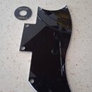 Černý plastový plech ochranný (pickguard) s několika otvory pro šrouby. Vedle něj je umístěn malý kulatý černý přepínač s bílým nápisem RHYTHM a TREB…