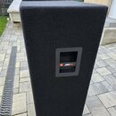 Dvě černé reproduktorové bedny potažené plstěným materiálem. Na přední straně je umístěn obdélníkový otvor s mřížkou a nápisem JBL JRX100. Povrch mat…
