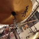 Zlatý činely s nápisem Zildjian. Činely jsou umístěny na chromovaných stojanách v interiéru místnosti. Povrch hlavního činely vykazuje mírné nepatnos…