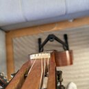 Detailní pohled na hřifo-tělo akustické kytary v hnědém dřevěném provedení. Vidět je bílý kostěný nebo plastový kobylníkový můstek a struny. Na kytar…