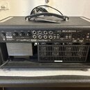 Zadní strana černého kytarového zesilovače s nápisem MESA/BOOGIE PETALUMA, CA USA. Jsou zde vidět různé ovládací prvky, konektory a přepínače, včetně…