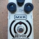 Bílý kytarový efekt pedál s nápisy MXR a Wylde OVERDRIVE. Obsahuje tři černé ovládací knoflíky s popisky OUTPUT, TONE a GAIN. Na šasi je viditelný po…