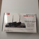 Krabice s bezdrátovým mikrofonním systémem. Na obalu je nápis AMERICAN AUDIO WM-219 a 2-Channel UHF Wireless Microphone System. Fotografie na krabici…