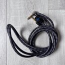Kabel s dvěma 6,3mm jack konektory v zlatém provedení. Kabel má černý textilní opletení s modrými detaily a je svázán černým suchým zipem. Na konekto…