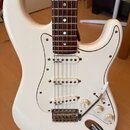 Bílá elektrická kytara typu Stratocaster s bílým pickguardem a hnědým hmatníkem. Nástroj má tři snímače typu single-coil, tři ovládací knoflíky a třy…