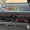 Míchací pult v černé barvě umístěný v transportním kufru. Na horní straně jsou viditelné posuvníky, knoflíky a nápisy SOUNDCRAFT Si EXPRESSION. V pře…