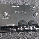 Černý zvukový interface Line 6 UX2. Na horní straně jsou čtyři chromované otočné ovladače s nápisy MIC 1/L GAIN, MIC 2/R GAIN, OUTPUT a PHONES. V pře…