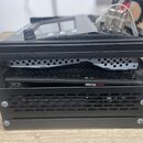 Černý kovový rám s perforovanými panely, uvnitř kterého jsou vidět elektronické součástky a kabeláž. V horní části je umístěno zařízení s displejem,…