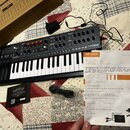 Černý syntetizátor s klaviatura, na jehož pravé straně je bílý nápis MINIFREAK. Vedle nástroje leží oranžovo-bílý návod s nápisy ARTURIA, MiniFreak a…