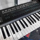 Černý digitální syntetizátor s klávesnicí. Na ovládacím panelu jsou viditelné nápisy OPERATOR SELECTS COPY, OPERATOR ON-OFF a FRACTIONAL MICRO TUNE.…