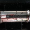 Detail stříbrné flétny v černém etui. Na nástroji je vyryto logo tvořené trojúhelníky a text SANKYO FLUTES MFG CO JAPAN. Vedle nápisu je viditelné oz…