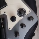 Detail elektrické kytary v šedé a krémové barvě. Na krémovém panelu jsou tři černé oválkové knofíky a jeden velký černý knofík s bílým nápisem PUSH P…