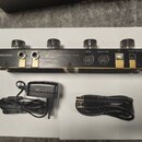 Černý MIDI kontrolér s nápisy HOTONE a AMPERO CONTROL. Zařízení má čtyři ovládací knoflíky, dva vstupy jack, konektory MIDI IN a MIDI OUT/THRU, USB p…