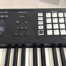 Detail ovládacího panelu černé klávesové nástroje s bílými a černými klávesami. Panel obsahuje sekce označené nápisy ARP/RHYTHM, SEQUENCER a SAMPLER…