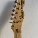Fotografie zachycuje hlavu kytary z přírodního světlého dřeva s chromovanými ladičkami. Na hlavě je černý nápis Fender, TELECASTER a THINLINE. Dále j…