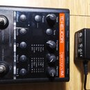 Černý efektový pedál s oranžovým nápisem TC HELICON harmony M. Zařízení má dva stoupací spínače, čtyři tlačítka a čtyři otočné ovladače s popisky Inp…