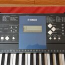 Černý digitální klavír značky YAMAHA s bílými klávesami. Na ovládacím panelu jsou viditelné nápisy MUSIC DATABASE, LESSON a SONG spolu s různými ovlá…