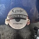 Detailní záběr na kovový štítkový nápis na modrém bubnu s metalickým povrchem. Na štítku je logo pdp a nápisy PLATINUM SERIES, Pacific Drums & Percus…