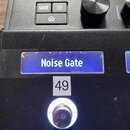 Detailní záběr na ovládací panel černého elektronického zařízení. Na modrém displeji je viditelný nápis Noise Gate a vedle něj začátek slova Legen. P…