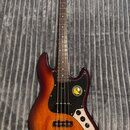 Čtyřstrunná elektrická basová kytara s tělem v barevně sunburst a černým pickguardem. Na hlavě hředu je viditelné žluté logo, na pickguardu se nacház…