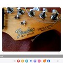 Detail hlavy kytary v přírodní dřevěné barvě s kovovými ladičkami. Je na ní vidět logo Fender, nápis STRATOCASTER a text MADE IN U.S.A. Dále je uvede…