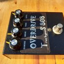 Černý kytarový efekt s nápisem OVERDRIVE TS 808 a doplňkem true bypass. Na horní straně jsou čtyři černé otočné knoflíky s kovovými vršky a popisky L…