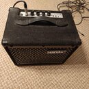 Černý basový kombo zesilovač potažený látkovým povrchem s kovovou mřížkou. Na přední straně je logo Warwick AMPLIFICATION a na horním ovládacím panel…