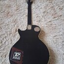 Zadní strana černé elektrické kytary s tvarem typu Les Paul. Na zadní části těla je nalepená nálepka s logem a nápisem DUNLOP STRINGS. Na horní části…