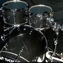 Sada černých bubnů značky SONOR s kovovým hardwarem. Na fotce jsou vidět tři tom-tomy a basový buben, z nichž na jednom je čitelně nápis SONOR. Vedle…