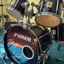 Černá bicí souprava s chromovaným kováním. Na basovém bubnu je bílý nápis SONOR a pod ním rukopisný bílý text Fanny Black. Na tomu
tomu bubnu jsou vi…