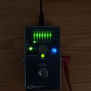 Šedý kovový efekt pedál s nápisem PROGRAMMABLE LED a logem SOURCE AUDIO. Zařízení má několik zelených svítících LED diod v mřížce, jeden modrý svítíc…
