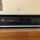 Černý výkonový zesilovač v hliníkovém racku. Na předním panelu je bílý nápis QSC AUDIO a model RMX 1850HD PROFESSIONAL POWER AMPLIFIER. Vpravo jsou o…