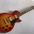 Elektrická kytara s tónem sunburst (červeno-žlutý přechod) a černým pickguardem. Na hlavě hředu je viditelné zlaté logo Gibson. Nástroj má dva humbuc…