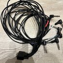 Černý kabel s více větvemi, který končí v jednom bodě širokým konektorem. Na druhé straně jsou čtyři 6,3mm jack konektory. Dvě z větví mají v části u…