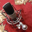 Stříbrný kondenzátorový mikrofon s černou mřížkou, umístěný v odpružíného držáku stejné barvy. Na těle mikrofonu je nápis CL7 STUDIO CONDENSER. Povrc…