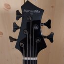 Černá hlava pětystrunné basové kytary s nápisem Marcus Miller M5. Jsou vidět pět ladicích kolíků a struny. Povrch je hladký a lesklý bez viditelných…
