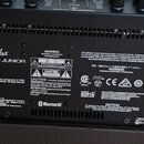 Zadní strana černého komba s nápisem Fender ACOUSTIC JUNIOR. Na zadním panelu jsou umístěny napájecí zásuvka, vypínač a různé konektory včetně USB a…