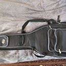 Černý polstrovatý pouzdro (gig bag) na hudební nástroj s bílým lemováním hran. Má ramenní popruh a velkou přední kapsu se zipem. Na horní části je vi…