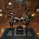 Elektronická bicí souprava značky Roland s černým rámem a chromovanými pady. Na basovém bubnu je bílý nápis Roland a pod ním menší nápis V-Drums. V p…