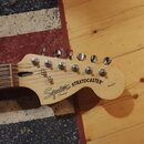 Hlava kytary z přírodního dřeva s šesti ladicími kolíky. Na hlavě je černý nápis Squier by Fender STRATOCASTER a menší nápis Standard. Povrch dřeva v…
