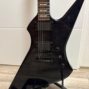 Černá elektrická kytara s ostrou, asymetrickou formou těla. Nástroj má dva humbuckery s nápisem EMG a jeden ovládací knoflík. Kytara je umístěna na č…